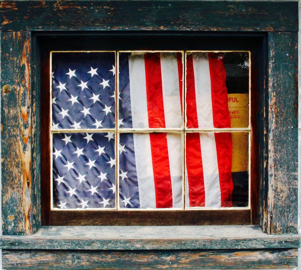An American flag hanging behind a rustic window